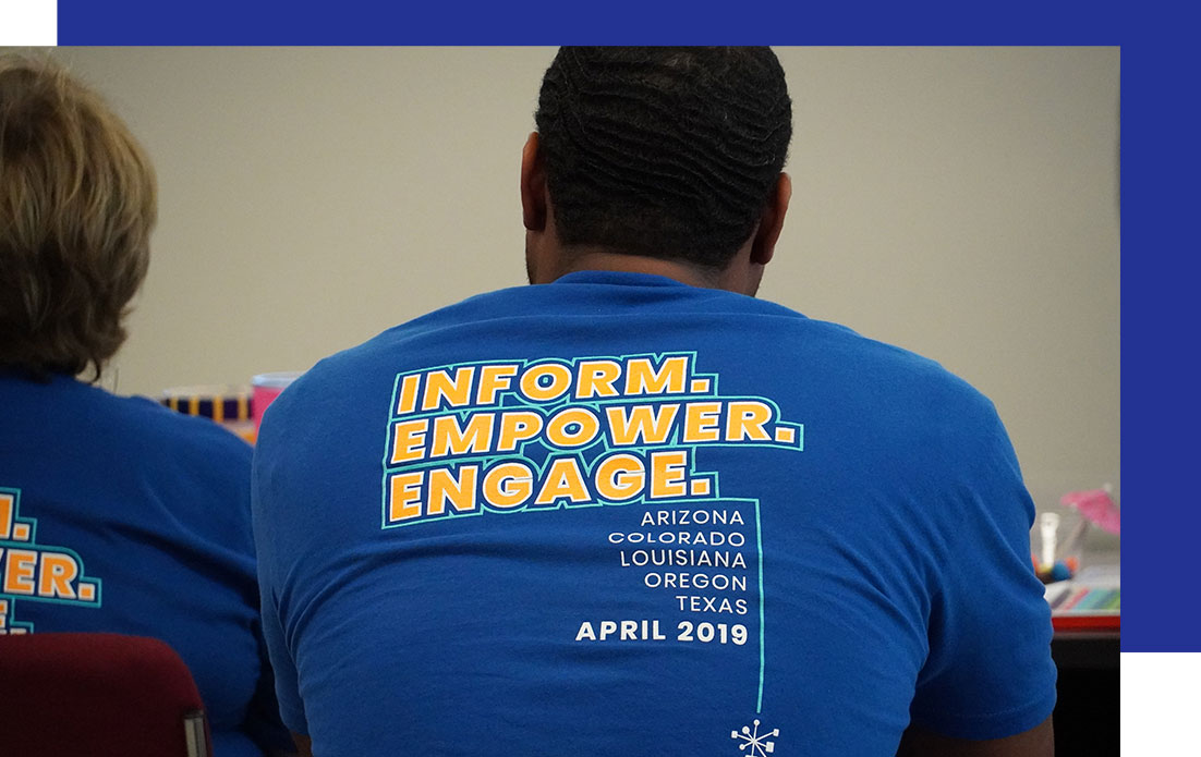 Two people in blue shirts sit at a table, one displaying "INFORM. EMPOWER. ENGAGE."