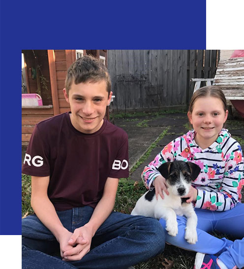 Access-Sciences-Blog-Supporting-Working-Moms-STAR-STEFKA-BORG-2 Two children sit on the grass, smiling as the girl pets a black and white puppy.