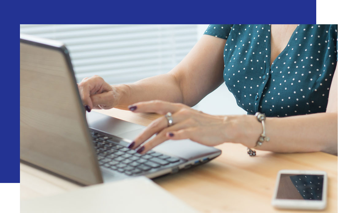 A woman in a green polka dot dress types on a laptop, exploring AI for business. A smartphone sits nearby.