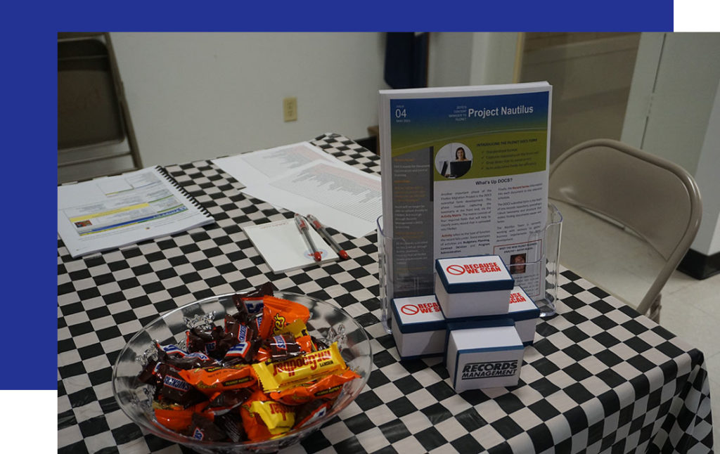 Access-Sciences-in-Baton-Rouge3 A checkered table holds candy, pamphlets, and Records Management boxes, promoting CRM Certification in Baton Rouge.