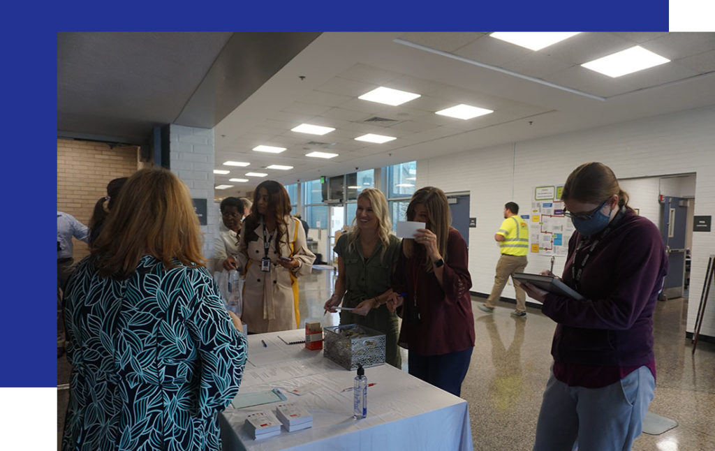 Access-Sciences-in-Baton-Rouge5 A group gathers around a table with papers and supplies in a bright hallway, engaging in Records Management discussions.