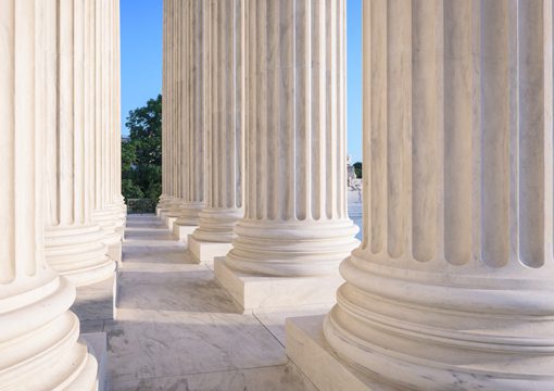 Large white marble columns in a row, with sunlight casting shadows on the floor, evoke the timeless strength seen in the Chemicals Industry. Green trees and blue sky are visible in the background.
